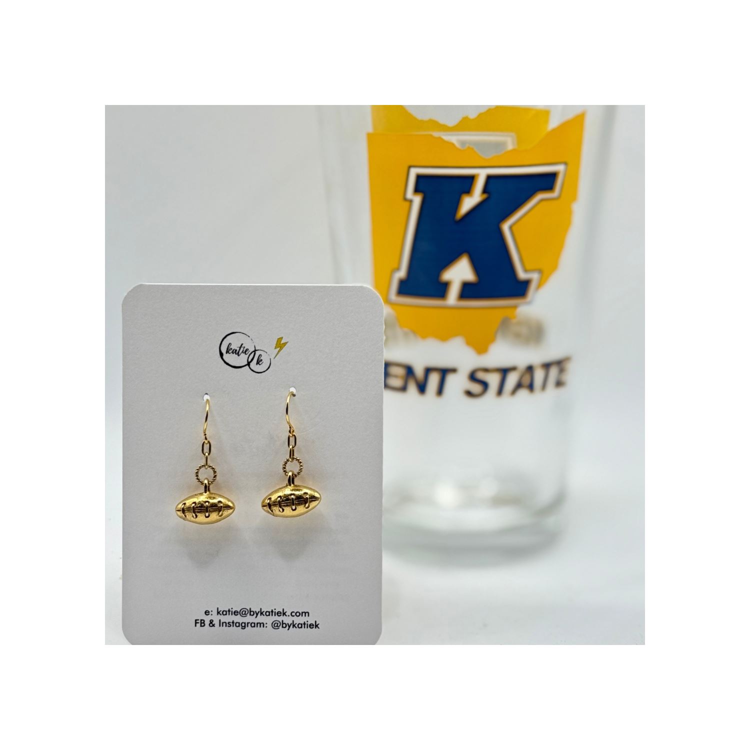 Mini Antique Gold Textured Football Earrings displayed on a card with a Kent State branded glass in the background.